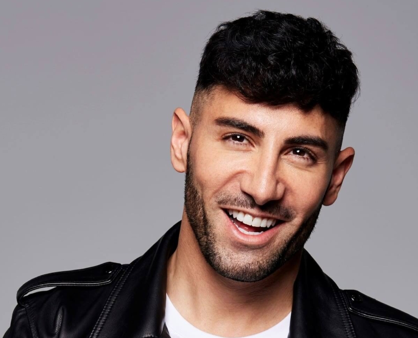 Das Profilbild von Ayan Yaruk bei der Redneragentur PODIUM – Ayan Yaruk lächelt in die Kamera, trägt eine schwarze Lederjacke und weißes Shirt vor grauem Hintergrund.