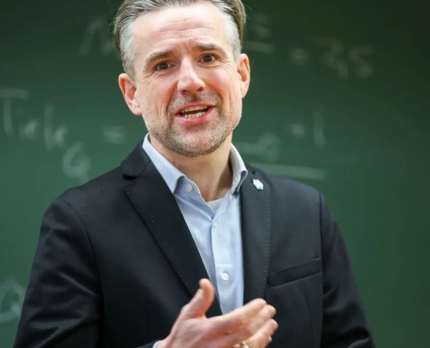 Mann spricht vor Tafel im Klassenzimmer.