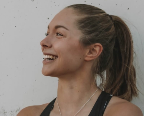 Gina Lückenkemper, deutsche Sprinterin, lächelnd im schwarzen Trainingsoutfit im Profilbild bei der Redneragentur PODIUM.