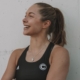 Gina Lückenkemper, deutsche Sprinterin, lächelnd im schwarzen Trainingsoutfit im Profilbild bei der Redneragentur PODIUM.