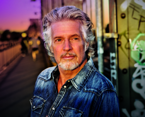 Das Profilbild von Frank Schätzing bei der Redneragentur PODIUM zeigt ihn vor einer urbanen Kulisse mit Graffiti und Sonnenuntergang – ein ausdrucksstarkes Porträt des bekannten Redners.