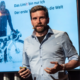Das Profilbild von Jonas Deichmann bei der Redneragentur PODIUM – als Redner auf der Bühne mit Präsentation im Hintergrund