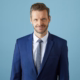 Das Profilbild von Florian Schroeder bei der Redneragentur PODIUM – professionell und sympathisch im blauen Anzug.