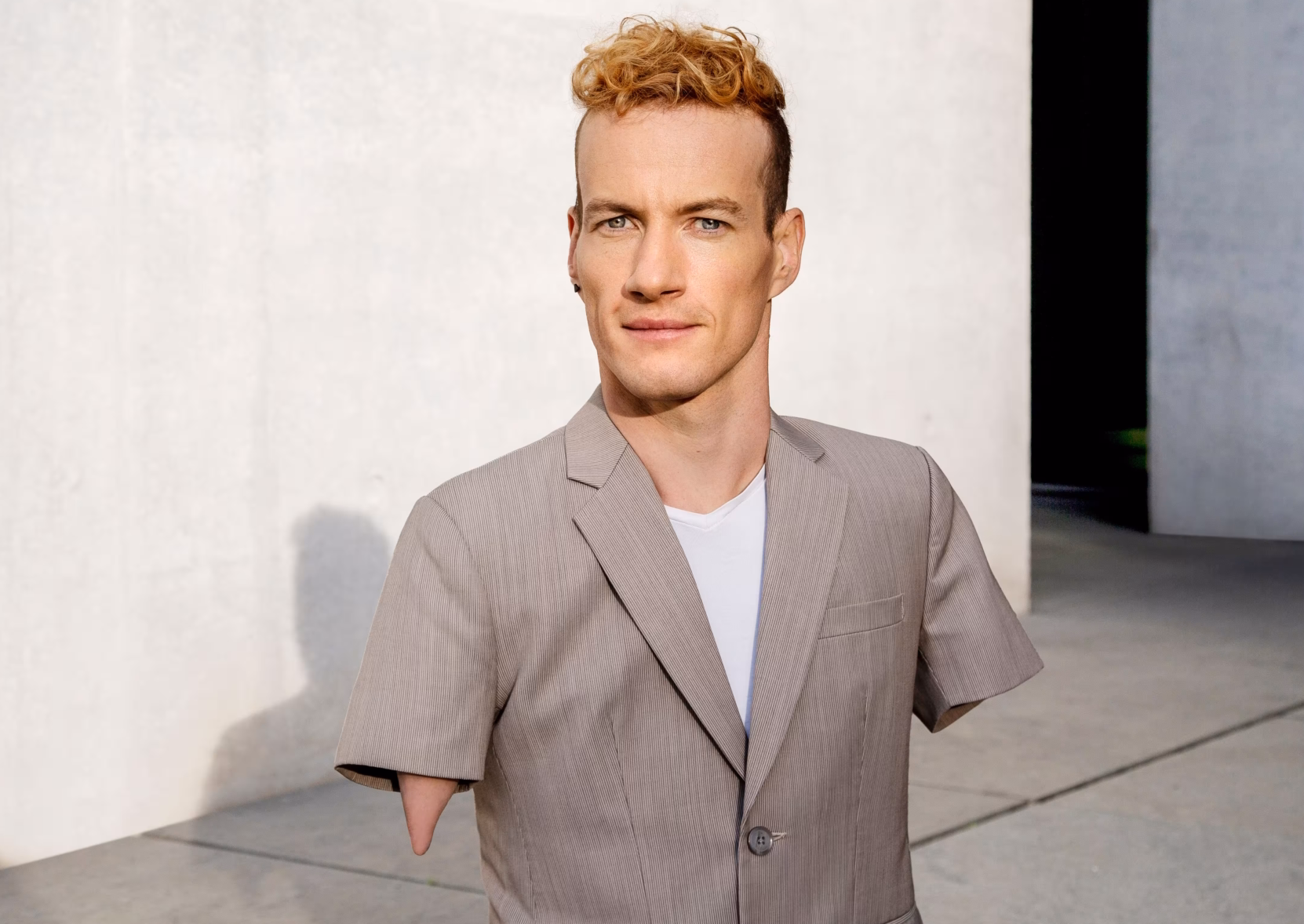 Das Profilbild von Janis McDavid bei der Redneragentur PODIUM zeigt den Redner in einem hellen Anzug vor moderner Betonarchitektur.