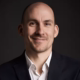 Jonas Geißler – Profilfoto bei der Redneragentur PODIUM in Businesskleidung mit dunklem Hintergrund