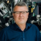 Maximilian Fichtner – Profilfoto bei der Redneragentur PODIUM vor einem technischen Hintergrund
