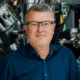 Maximilian Fichtner – Profilfoto bei der Redneragentur PODIUM vor einem technischen Hintergrund