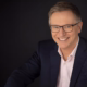 Norbert König – Profilfoto bei der Redneragentur PODIUM mit dunklem Hintergrund und freundlichem Ausdruck