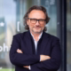 Peter Brandl im Business-Outfit mit verschränkten Armen vor einem modernen Glasgebäude – das Profilbild bei der Redneragentur PODIUM